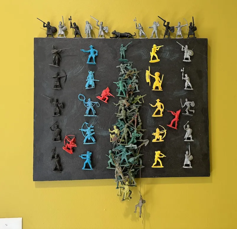 Plastic toy Cowboys and Indians, along with plastic toy Saxons, Astronauts, WW I & WW II figures with a black leopard sitting on the top of the canvas along with Saxons and Astronauts.